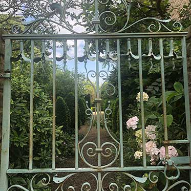 Looking through a garden gate along a long path leading through a garden